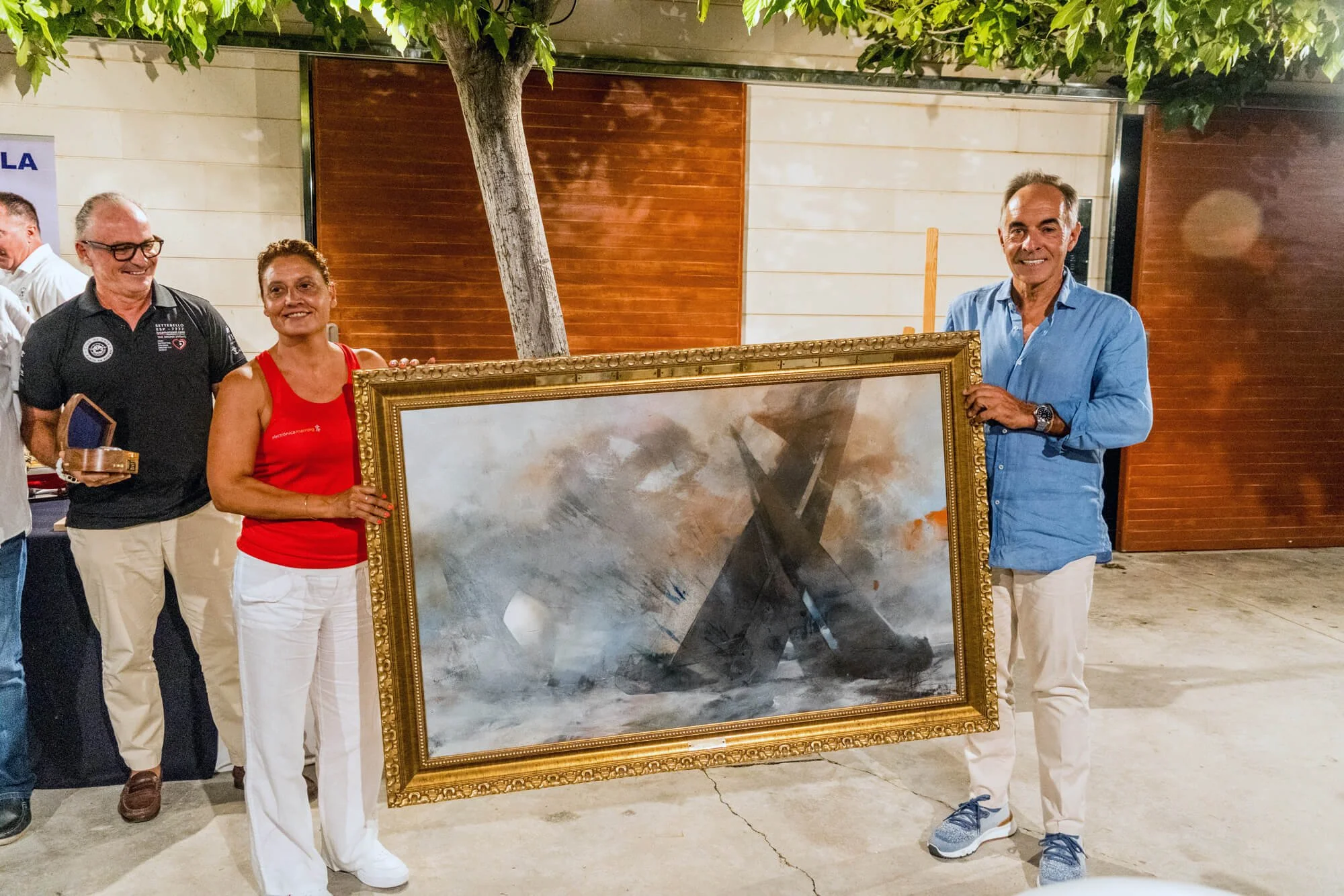 Personas en una reunión sosteniendo un cuadro con una pintura abstracta y sonriendo.