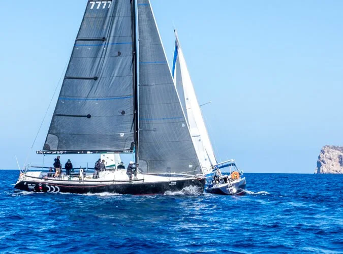 Velero navegando en el mar con varios tripulantes y una isla a lo lejos.