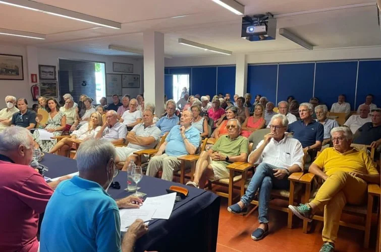 Reunión de adultos mayores en una sala, algunos toman notas y otros escuchan.