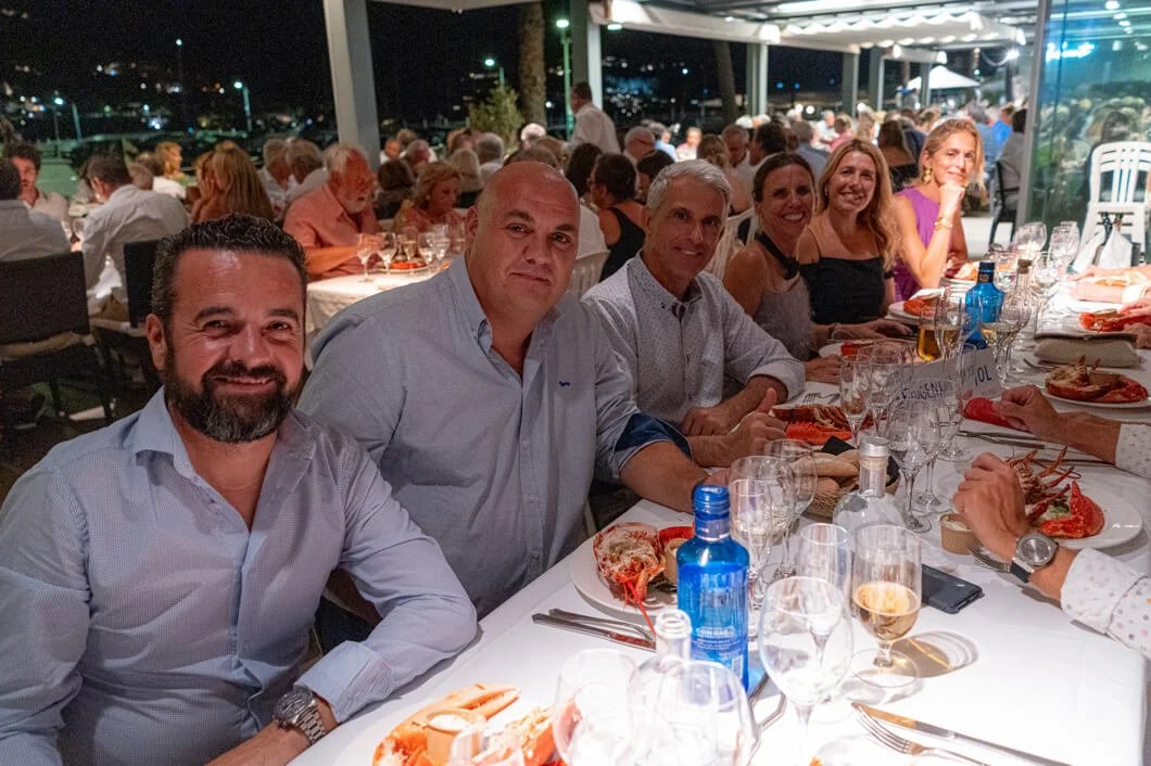 Grupo de personas en una cena elegante, sentadas en una mesa con comida y bebidas, en un restaurante al aire libre por la noche.