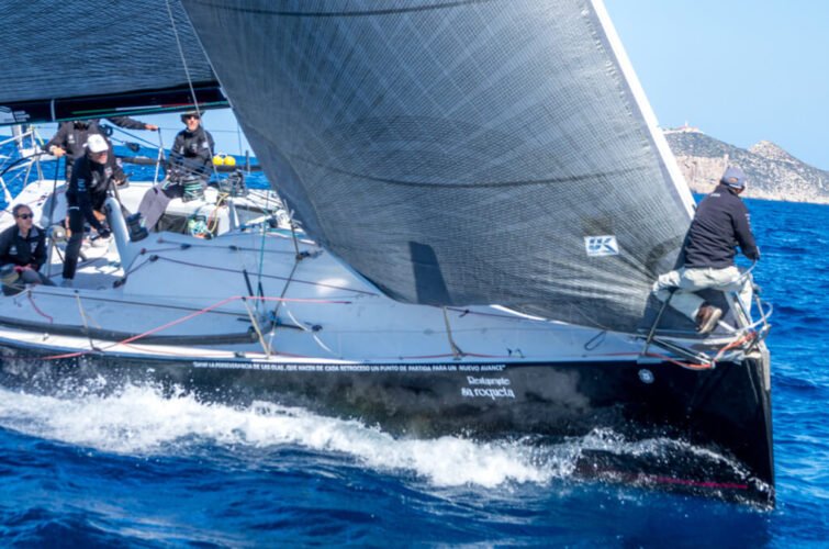 Un velero navegando a toda velocidad en el mar con varias personas a bordo ajustando las velas.