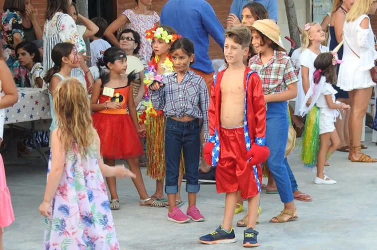 Niños disfrazados en una celebración al aire libre, algunos con accesorios como sombreros y ropa temática, rodeados de adultos y otros niños.