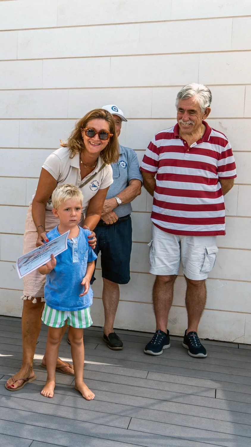 Grupo de cinco personas, incluyendo un niño con un diploma, posando en una pared de fondo, sonriendo y disfrutando un momento juntos.