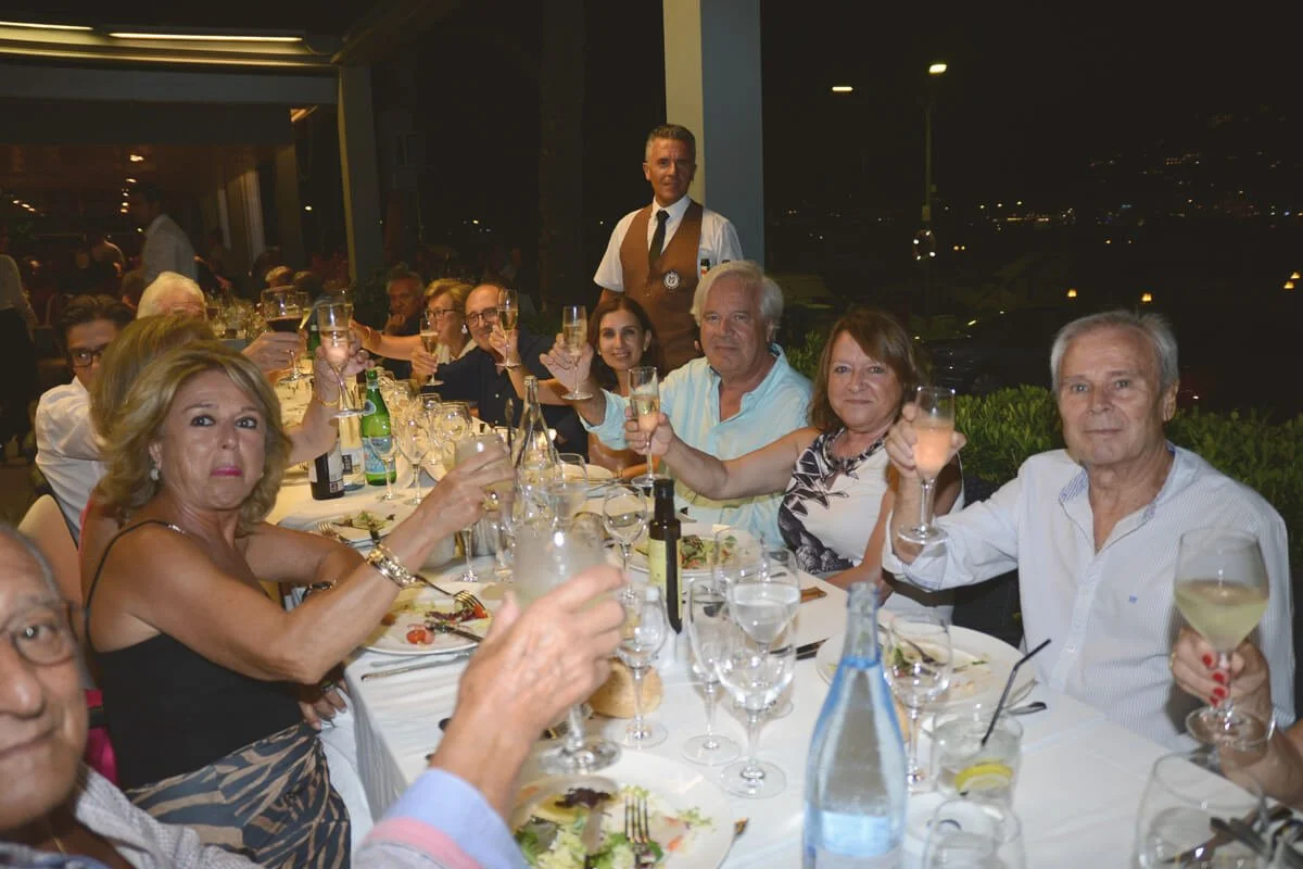 Personas sentadas en una mesa de cena celebrando, levantando copas con vino y bebidas, en un ambiente elegante y festivo