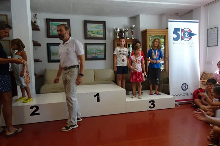 Niños en una ceremonia de premiación en un lugar cerrado con trofeos en exhibición y un banner del 50 aniversario del CVP.