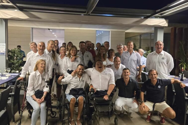 Grupo de personas sonriendo en un salón de restaurante, algunas en sillas de ruedas, celebrando una reunión o evento.