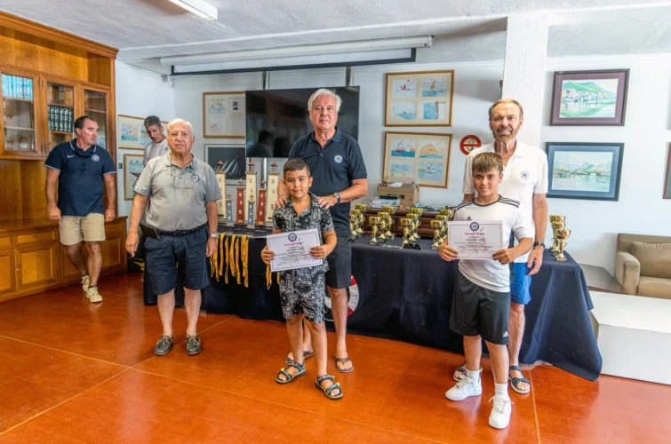 Niños recibiendo premios en una ceremonia en un salón, con adultos y diplomas.