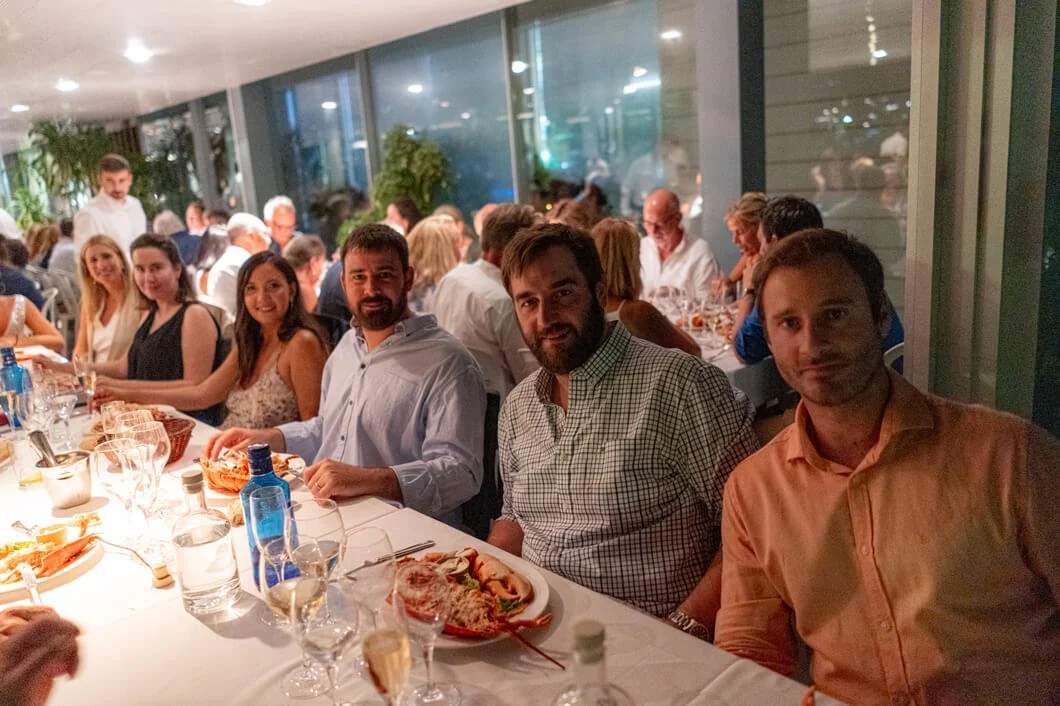 Grupo de personas cenando en un restaurante durante la noche, con platos y bebidas en la mesa.