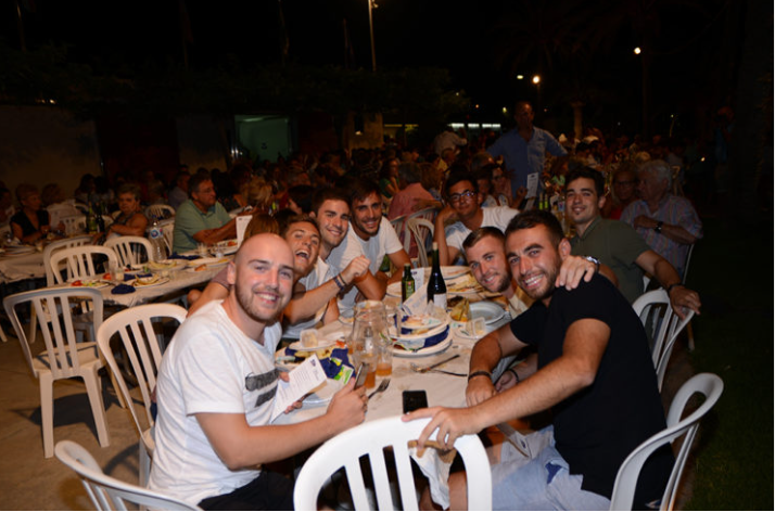 Grupo de amigos sonriendo y disfrutando en una cena al aire libre por la noche.