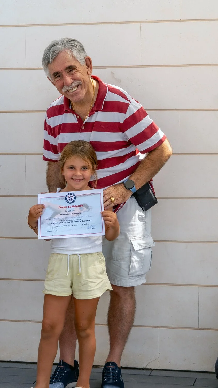 Un niño y un adulto posando juntos frente a una pared, el niño sostiene un certificado y ambos sonríen