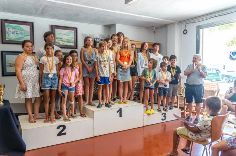 Niños en una ceremonia de premiación en un lugar cerrado, con algunos en el podio, recibiendo medallas y trofeos.