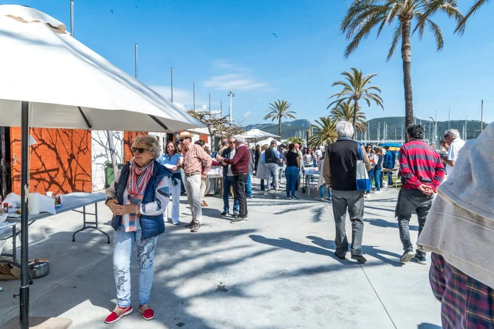 Gente en un mercado al aire libre junto a un muelle con palmeras bajo un cielo azul