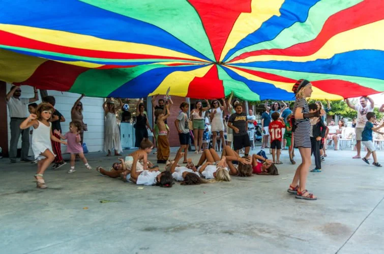 Niños y adultos jugando con un canopy de colores en un espacio abierto.