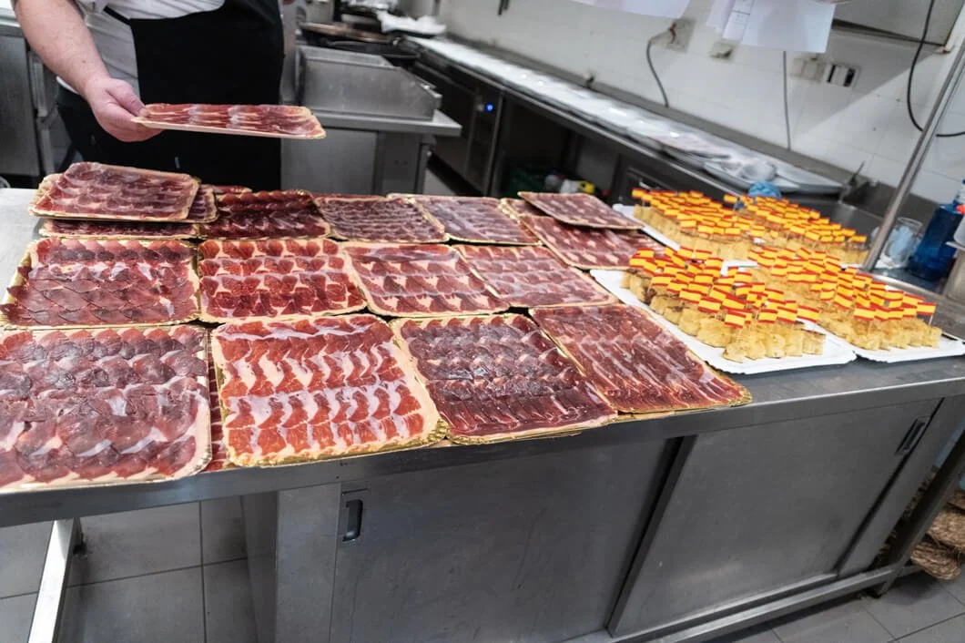 Tabla con diferentes tipos de jamón y queso en una cocina comercial.