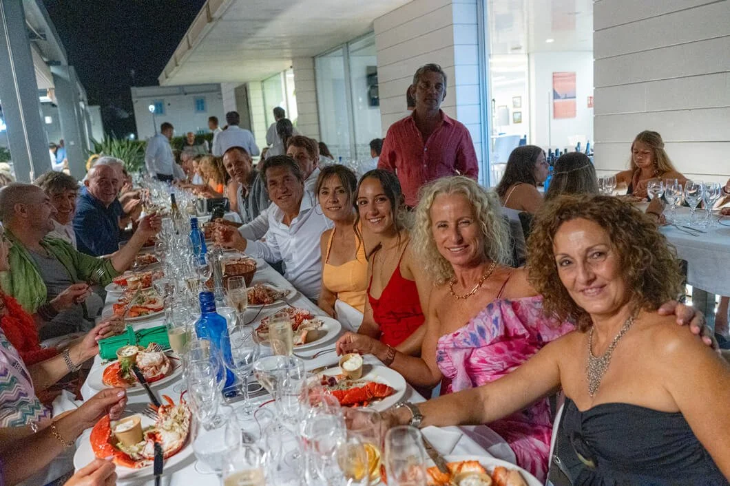Grupo de personas en una cena formal en un restaurante, disfrutando de comida y bebida, algunos sonriendo y posando para la foto.