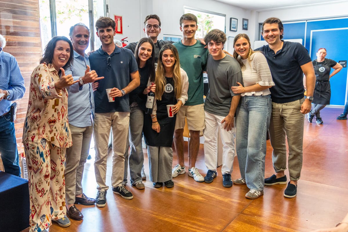 Grupo de jóvenes y adultos sonriendo y posando juntos en un ambiente interior, algunos con bebidas en las manos.