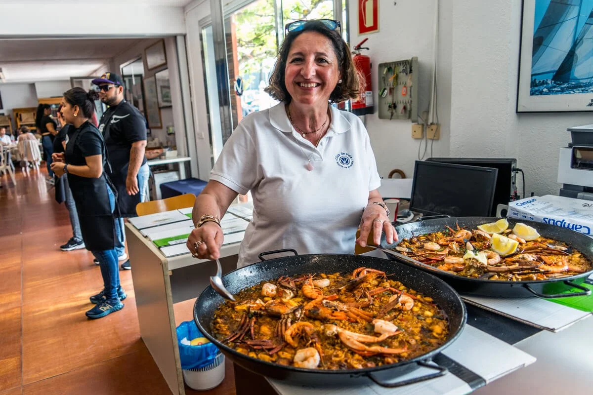 Mujer sonriendo con platos grandes de paella con mariscos en un ambiente interior