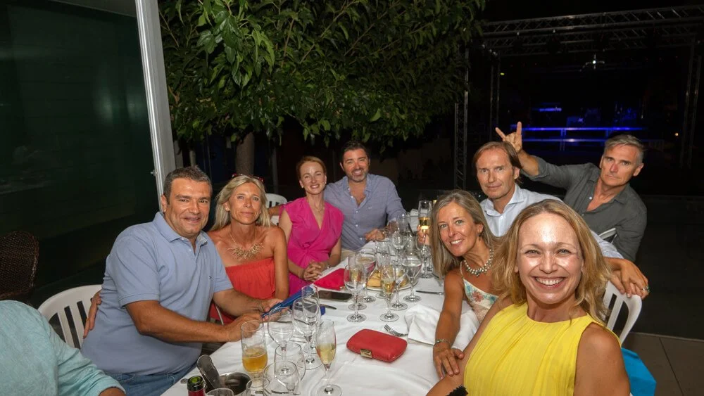 Grupo de personas en una mesa celebrando con comida y bebidas en un evento social al aire libre por la noche.