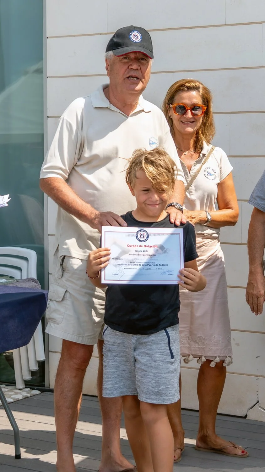 Niño sosteniendo un diploma de natación, acompañado por una mujer y un hombre, en un evento al aire libre.