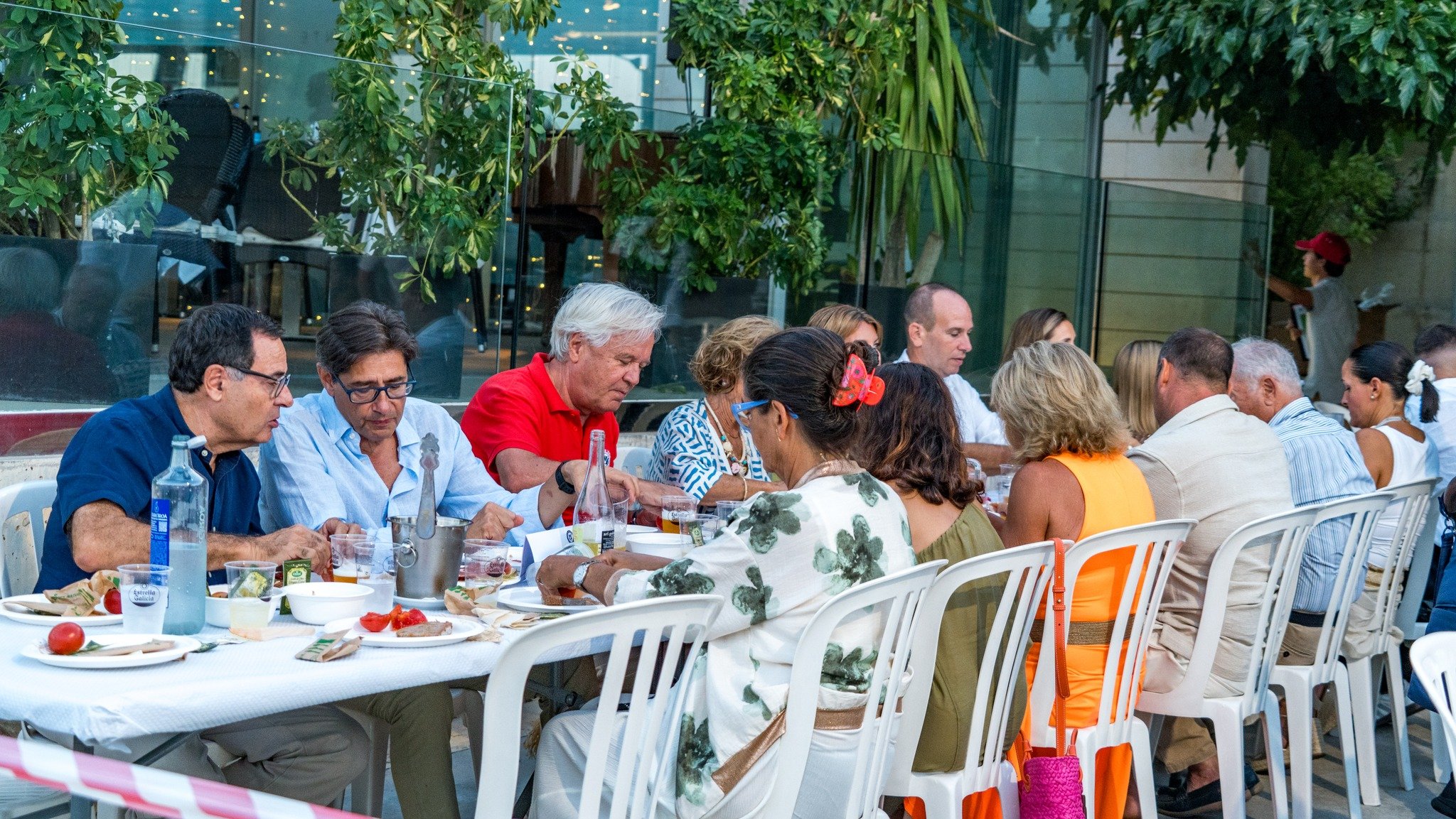 Grupo de personas sentadas en una mesa al aire libre disfrutando de una comida en un lugar con mucho verde y plantas