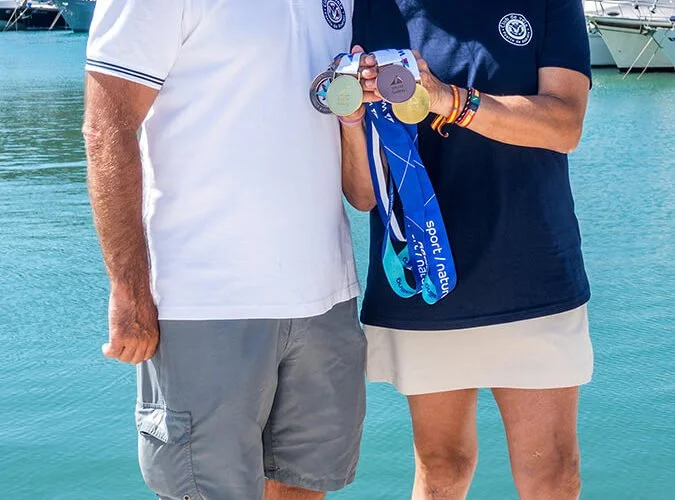 Personas mostrando medallas en un fondo de agua y barcos, celebrando logros deportivos.