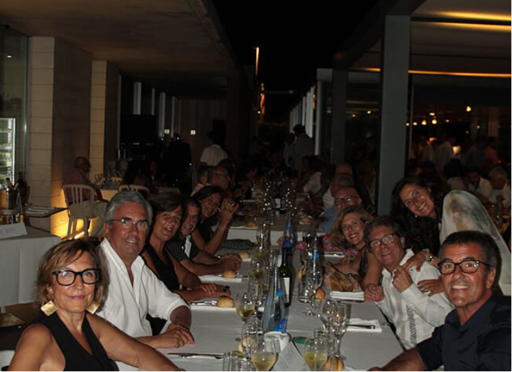 Grupo de personas celebrando en un restaurante, sentados alrededor de una mesa larga con comida y bebidas.