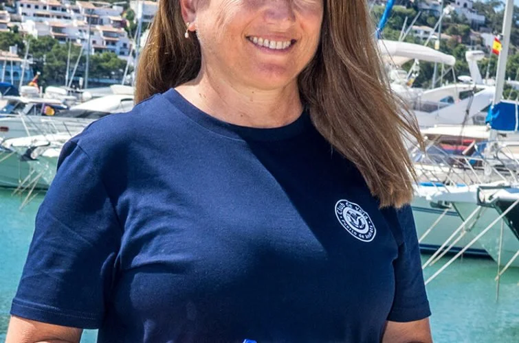 Mujer con camiseta azul en puerto con yates y barcos en el fondo.