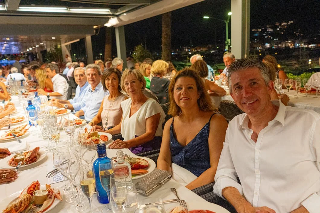 Grupo de personas sentadas en una mesa larga durante una cena en un lugar cerrado y elegante por la noche.