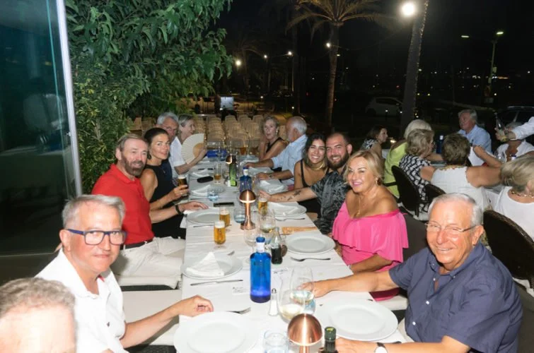Grupo de personas sentadas en una mesa al aire libre en la noche, disfrutando de una cena con bebidas y comida.