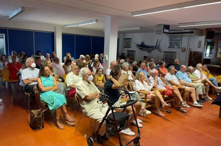 Personas sentadas en sillas en una sala, algunas usando mascarillas, participando en un evento o reunión.