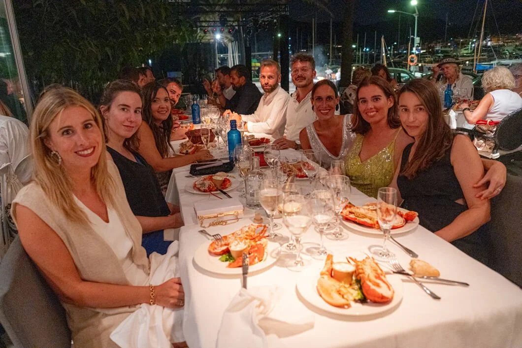 Grupo de personas sentadas alrededor de una mesa en un restaurante, disfrutando de una comida elegante en la noche, con platos de mariscos y bebidas. Ambiente festivo y elegante.
