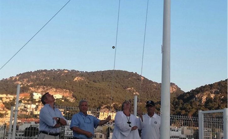 Cuatro personas controlando un cometa en un campo abierto con colinas verdes de fondo bajo un cielo despejado.