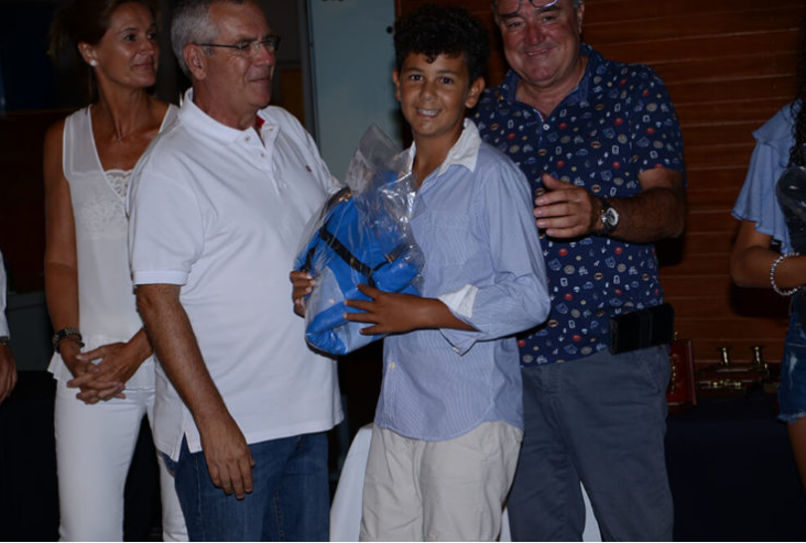 Un grupo de personas, incluyendo un niño con uniforme escolar, celebrando un logro o evento en un ambiente interior.