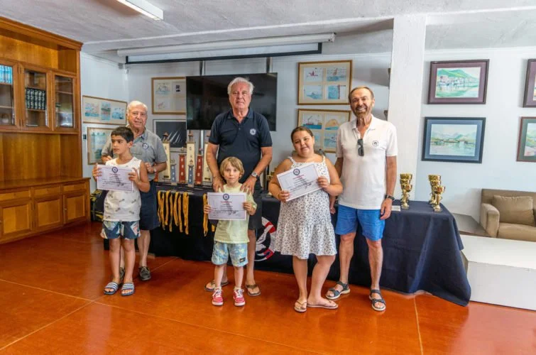 Grupo de cinco personas, incluyendo tres niños y dos adultos, en una sala con decoraciones y diplomas, posando para una foto en una ceremonia de premiación.