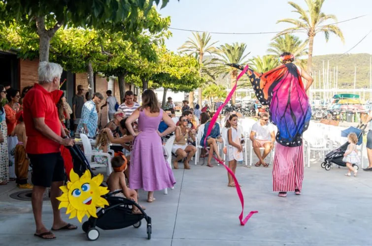Personas en un evento al aire libre, algunos niños, adultos, y una marioneta de mariposa gigante.