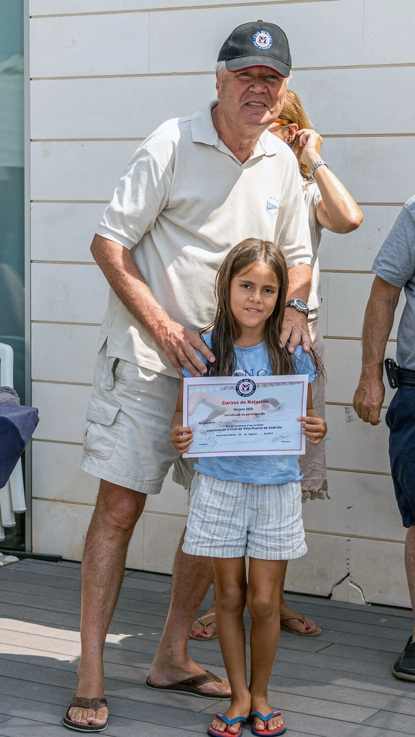 Niña sosteniendo un certificado en una ceremonia de natación, acompañada por un hombre mayor en un evento al aire libre.