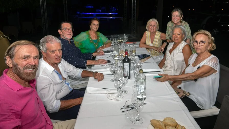 Grupo de personas sentado en una mesa de cena, con copas y botellas de vino, en un ambiente iluminado