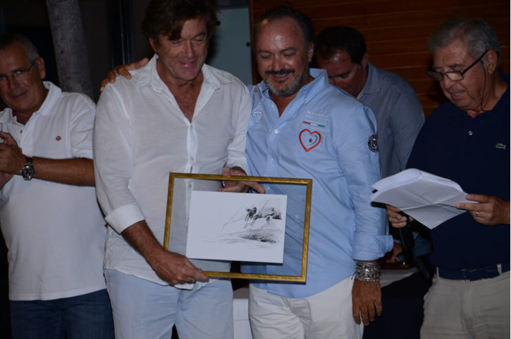Grupo de cinco hombres en una celebración, uno de ellos recibe un cuadro y todos sonríen, en un ambiente informal.