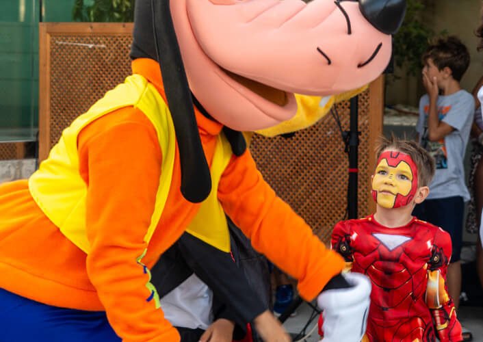 Un personaje disfrazado de Snoopy interactuando con niños, uno de los cuales está vestido de Iron Man, en una imagen en exteriores.