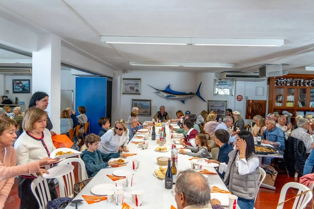Grupo de personas sentadas en una mesa larga en un comedor, con decoración marina en las paredes, incluyendo un pez espada gigante y cuadros, en un ambiente cálido y animado.