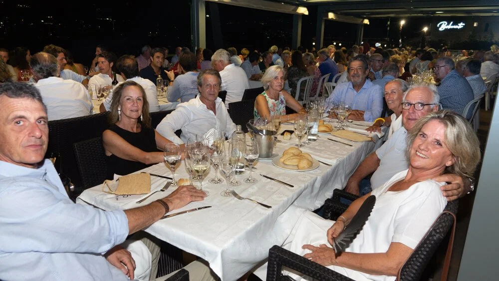 Grupo de personas en una cena formal en un restaurante con muchas mesas y comensales.