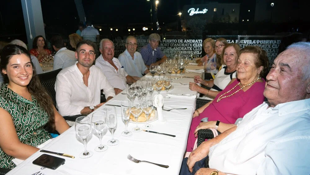 Grupo de personas sentadas en una mesa larga en un restaurante, posando y sonriendo para la foto.