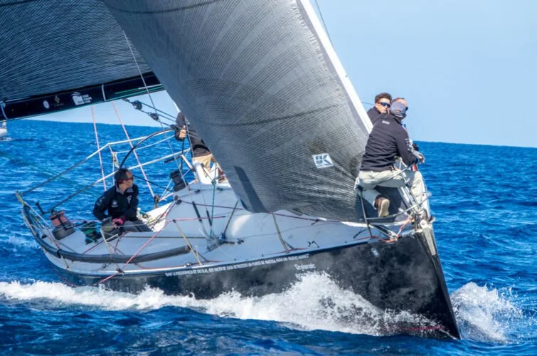Personas navegando en un velero en el océano azul con cielo despejado.