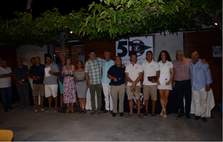 Grupo de personas en una celebración al aire libre, con un mural de fondo que conmemora el 50 aniversario.