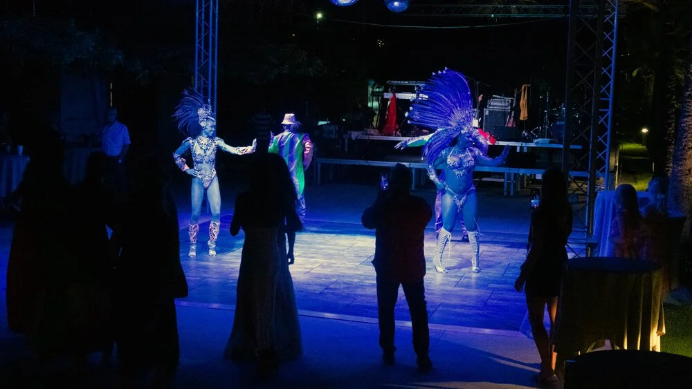 Espectáculo de baile con artistas disfrazados con trajes elaborados y plumas, iluminados con luces azules en un evento nocturno.