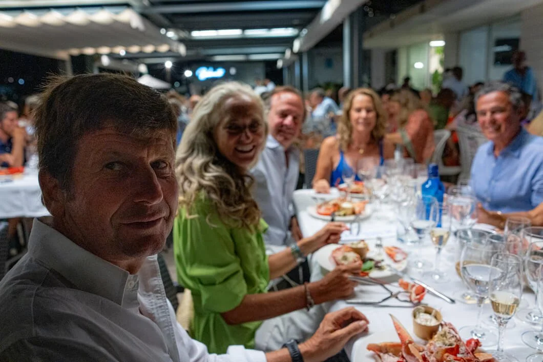 Grupo de personas cenando en un restaurante al aire libre durante la noche, con comida y bebidas sobre la mesa.