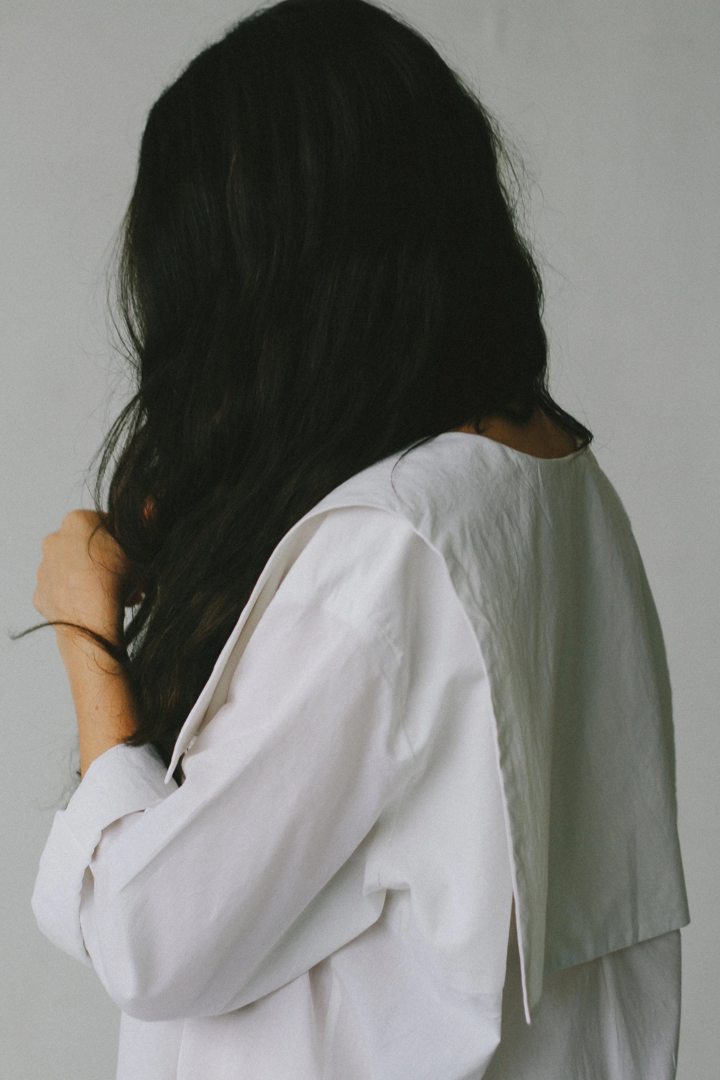 Une personne avec de longs cheveux noirs portant une chemise blanche, vue de côté, avec un fond gris clair.