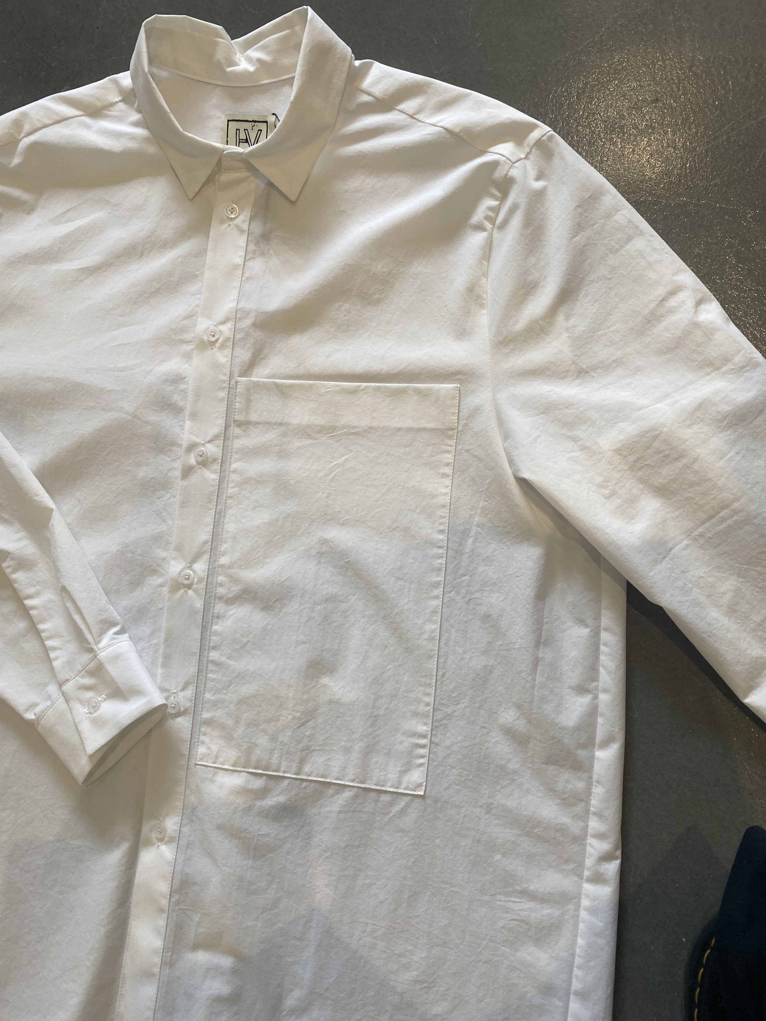 Chemise blanche à col classique avec boutonnière devant, posée sur une surface sombre.