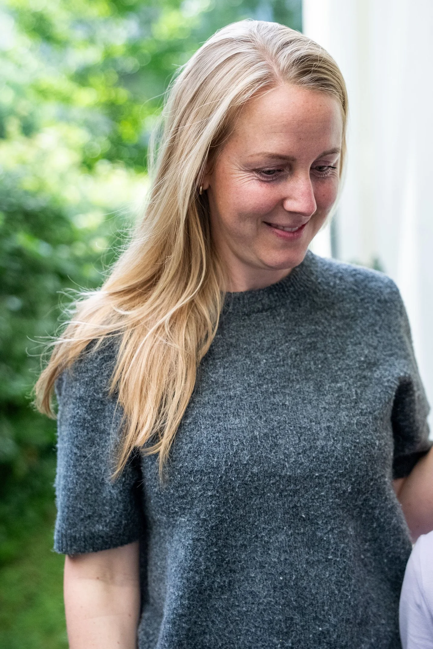 Nahaufnahme einer lachenden Frau mit blonden langen Haaren vor einem grünen, unscharfen Hintergrund.