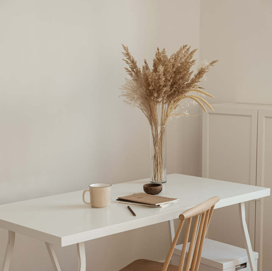 Ein Schreibtisch in heller Umgebung mit Tasse, Notizen und Blumen